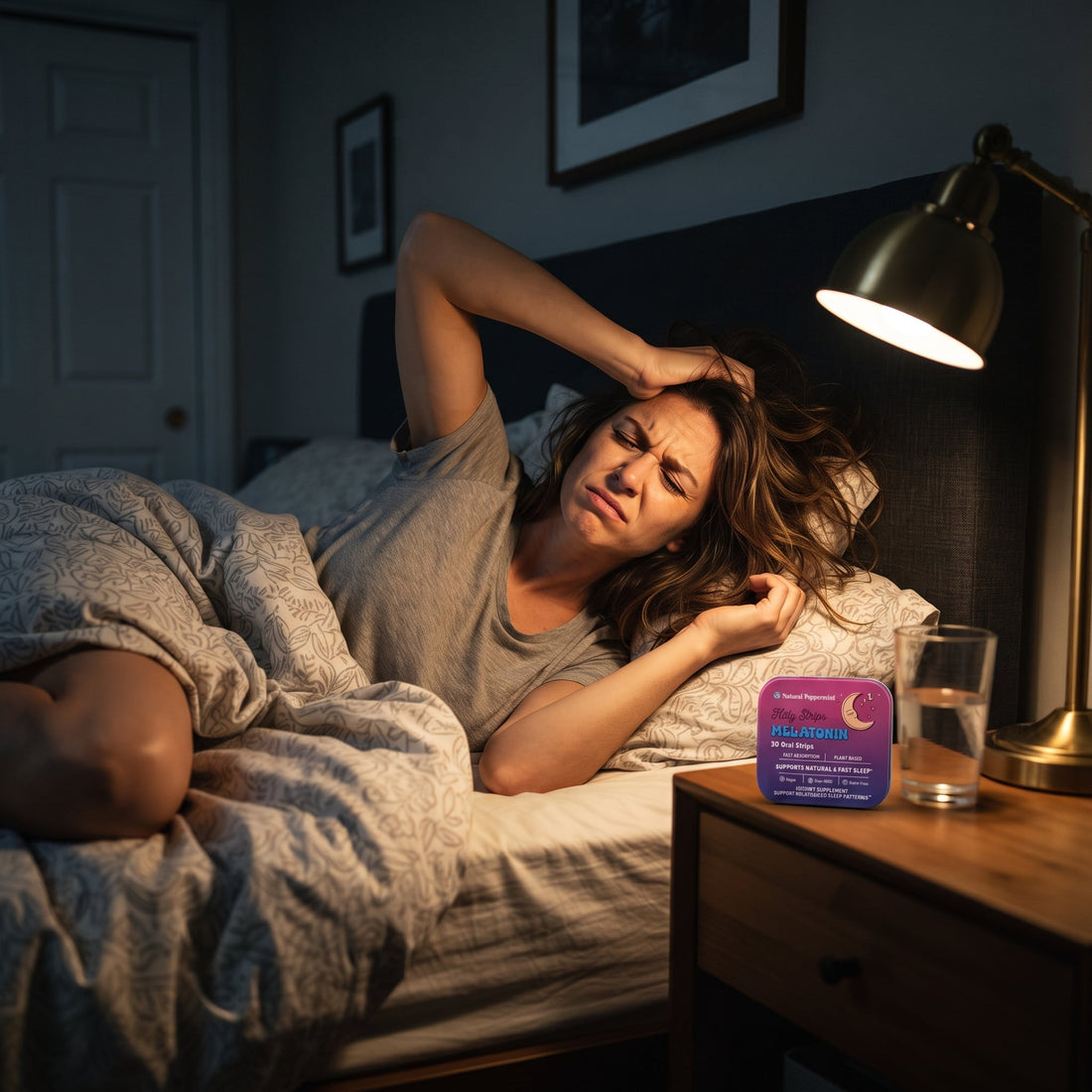 Frustrated woman lying awake in bed at night, gripping her hair in exhaustion, with a Holy Strips Melatonin tin on her nightstand.