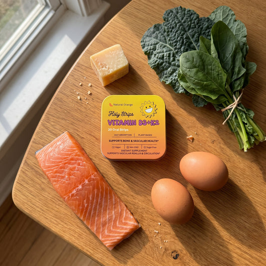 Holy Strips Vitamin D3+K2 tin on a wooden table surrounded by parmesan cheese, kale, spinach, salmon, and eggs.