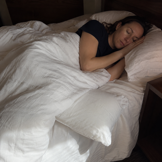 A woman sleeping on her side with a pillow tucked between her knees in a softly lit bedroom.