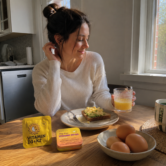 Woman eating breakfast with eggs and a glass of orange juice at a sunlit kitchen table.