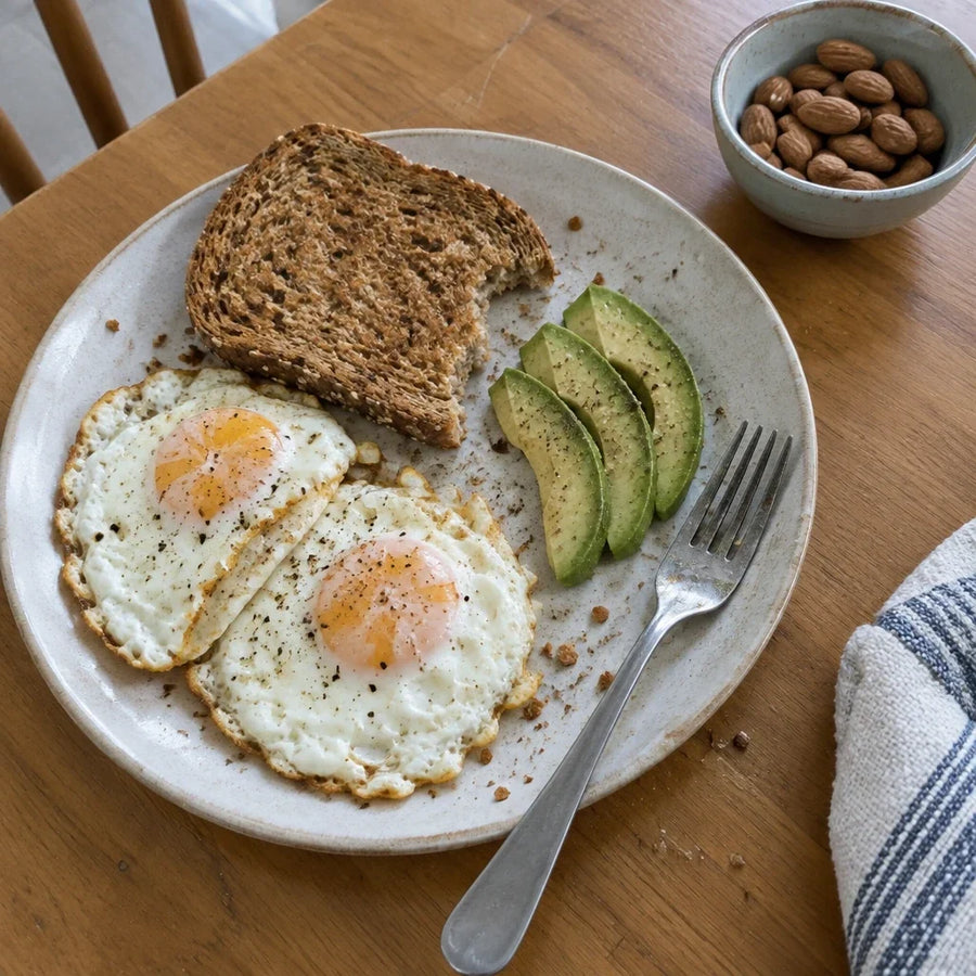 Eggs, wholegrain toast, and avocado on a plate with a small bowl of almonds.