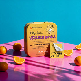 A yellow tin labeled HolyStrips® D3 + k2 by Holy Strips rests on a pink surface with sliced oranges and fast-dissolving strips for immune support nearby.