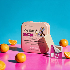 A box of HolyStrips® Biotin by Holy Strips is shown with its packaging, an open sachet, and sliced oranges on a vibrant pink and blue background. These fast-dissolving oral vitamin strips deliver convenient support for hair, skin, and nails in each biotin strip.