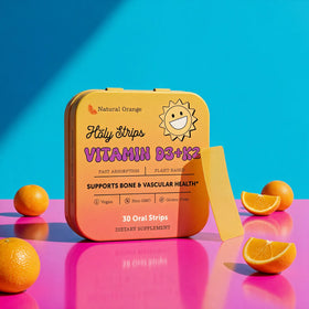 Square orange container of HolyStrips® D3 + k2 fast dissolving strips on a pink surface with orange slices, set against a blue background.