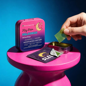 A hand holds a green HolyStrips® Melatonin Strip above an open tin labeled “Holy Strips” on a pink stool, with packaging that highlights sleep support benefits. These dissolvable strips from Holy Strips are designed as a fast-acting sleep aid to promote restful nights.